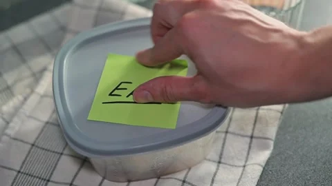 A hand places a sticky note with the word EAT on a container in a kitchen. The Stock Footage 339096782