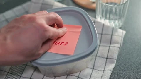 A hand places a sticky note yours on a food container to indicate ownership. The Stock Footage 339096785