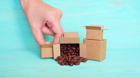 Hand Places Tiny Coffee Cup from Box into Coffee Bean Pile Stock Footage 297949884