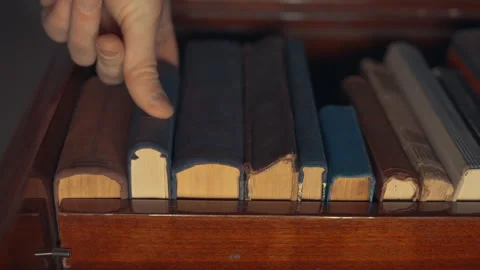Hand Placing Antique Book Back on Wooden Shelf: Close-Up Bottom-Up Angle View Stock Footage 339111484