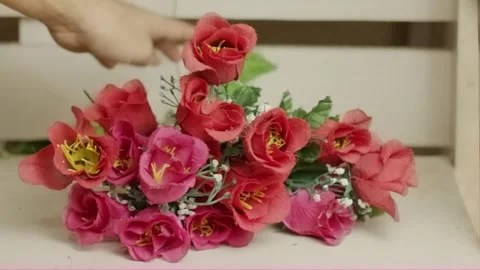 Hand placing artificial red roses on a clean white table Stock Footage 320127879