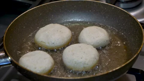 A hand is placing a ball-shaped dough on a boiling oil pan, a close-up view. Vidéo 265494375