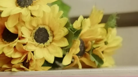 Hand placing bright artificial sunflowers on a white table Stock Footage 320127623