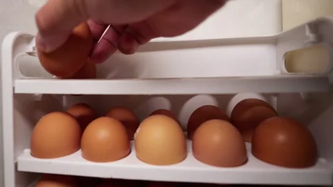 Hand placing brown egg in white holder, linking to grocery and food prices. Stock Footage 321634809