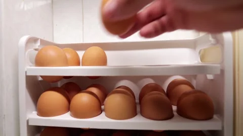 Hand placing brown egg in white holder, linking to grocery and food prices. Stock Footage 321634826
