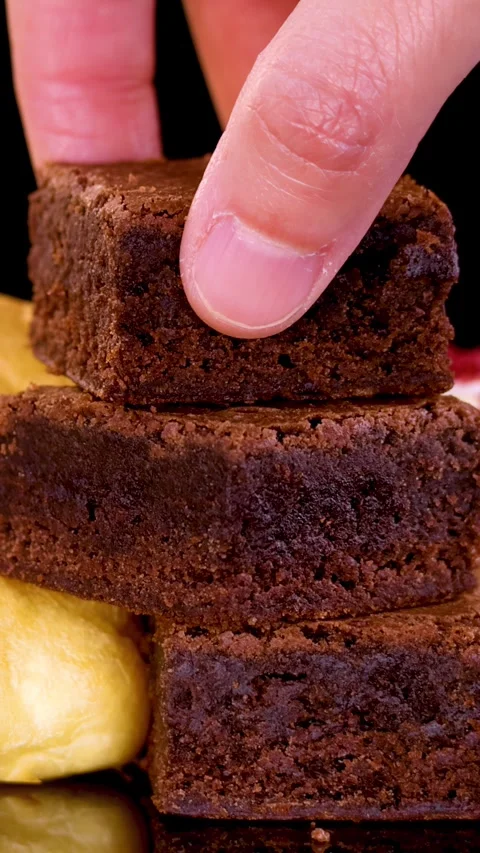 Hand Placing Brownie on Dessert Stack in Bakery Setting Stock Footage 315423468