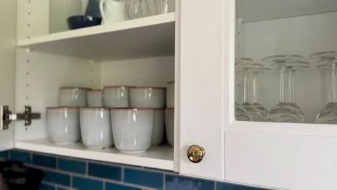 Hand placing ceramic cups inside white wooden kitchen wall cabinet Stock-Footage 336211586