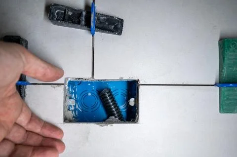 Hand placing ceramic tile around a blue electrical box, using a tile leveli.. Stock Photos