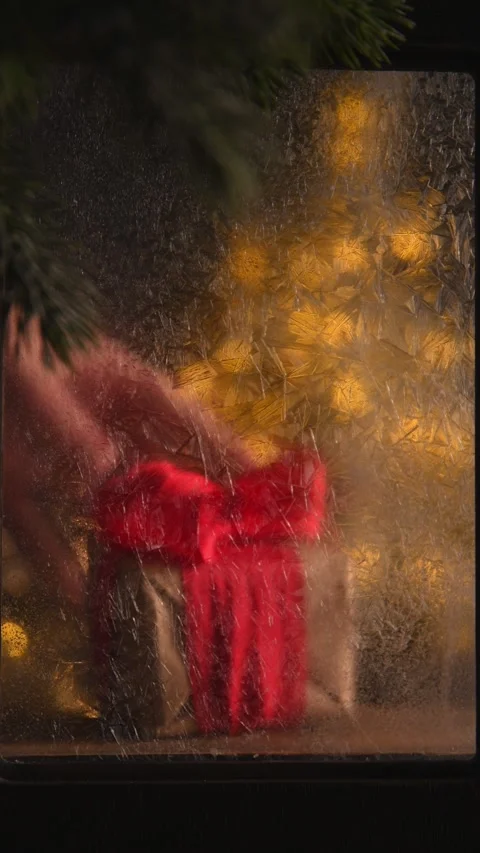 Hand is placing a christmas gift wrapped in red paper behind a frosted glass Stock Footage 295506803