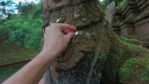 Hand placing coin on moss covered stone statue at Buddhist temple in Chiang Stock Footage 346025751