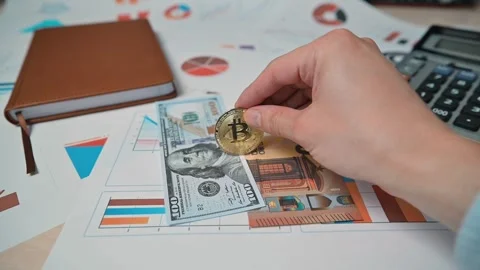 A hand is placing cryptocurrency coins next to banknotes on a table filled with 動画素材 338301534