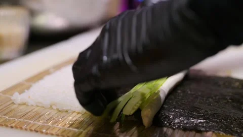 Hand placing cucumber strips and cream cheese onto seaweed with rice during Stock Footage 293520655
