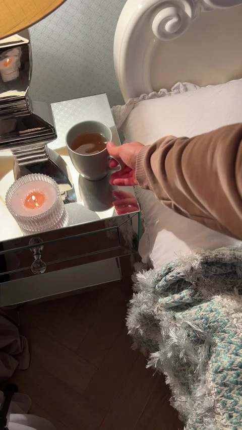 Hand placing cup of tea on mirrored nightstand in cozy bedroom Video stock 346094870