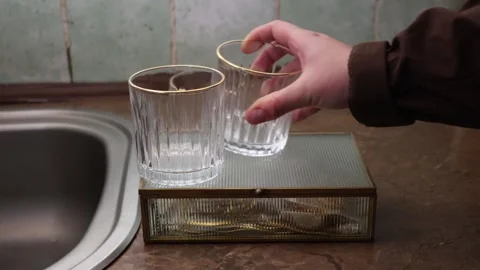 Hand placing delicate fluted glasses with gold rims on a decorative tray Stock Footage 339178531
