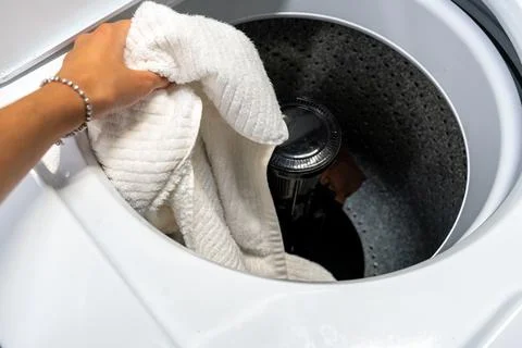 Hand placing dirty laundry into an open top-loading washing machine Foto stock