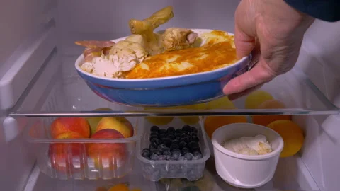 A hand placing a dish of dinner leftovers on a fridge shelf. Video stock 253198378