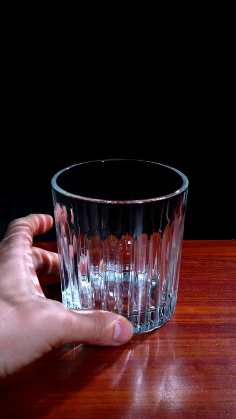 Hand Placing Empty Crystal Glass on Wood Table Dark Background Vertical Stock Footage 324597378