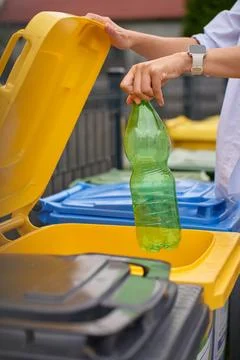 Hand placing empty plastic bottle into yellow recycling bin outdoors Stock Photos