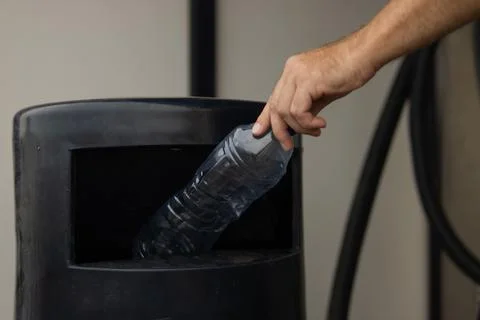 Hand placing empty plastic bottle into black recycling bin, promoting respo.. Stock Photos