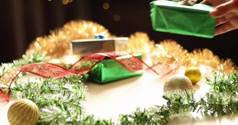 Hand placing a festive green gift box amidst Christmas decorations and ornaments Stock Footage 339072092