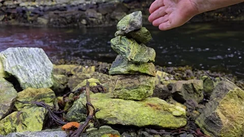 Hand placing the final stone on a balanced stone tower Stock Footage 344058619
