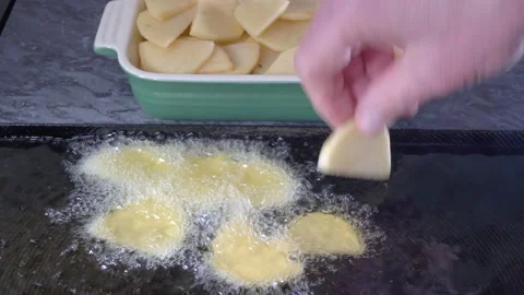 Hand placing the first raw potato slices into a pan of hot oil. Stock Footage 154407858