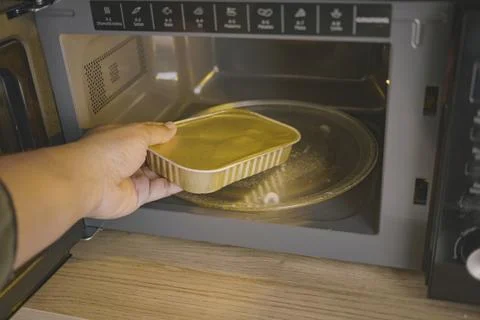 Hand placing food container inside microwave oven Stock Photos