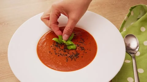 Hand placing fresh green basil leaf on  hot red tomato and pepper cream soup Stock Footage 341361387