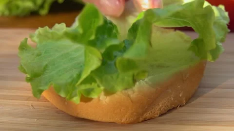Hand Placing Fresh Lettuce Leaf on Burger Bun Stock Footage 328092970