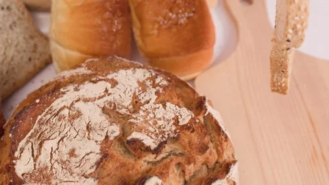 Hand Placing Fresh Multigrain Bread Slice on Wooden Cutting Board Stock Footage 337521179
