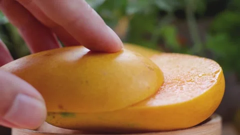 Hand placing a fresh slice of ripe yellow mango on a wooden board Stock Footage 341999962