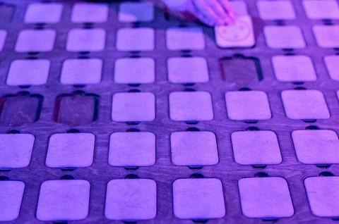 Hand placing game piece on patterned board with purple lighting Stock Photos
