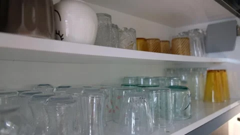 Hand Placing Glass on Shelf Inside Kitchen Cabinet with Two Rows of Glasses Video stock 302688057