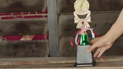 A hand placing a gold trophy with red and white ribbons on a wooden table a.. Stock Footage 324823047