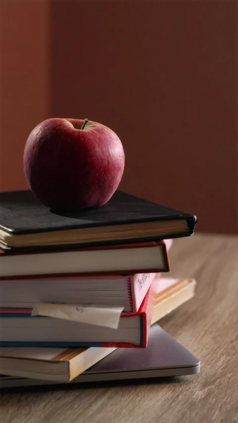 Hand placing green apple on stack of school textbooks vertical Stock Footage 340139112