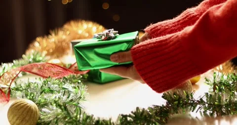 Hand placing a green gift box amidst festive Christmas decorations and lights Stock Footage 339073088