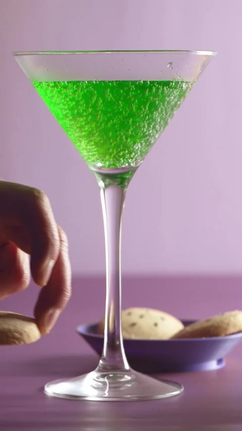 Hand placing a Halloween bat cookie against a glass with green liquid Stock Footage 343432614