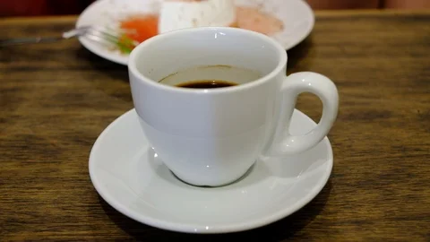 Hand placing hot ceramic coffee cup on saucer over wooden table in cafe Stock Footage 91928442