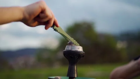 Hand placing hot coal on hookah bowl outdoors on a peaceful sunny day, relaxed Stock Footage 308521018