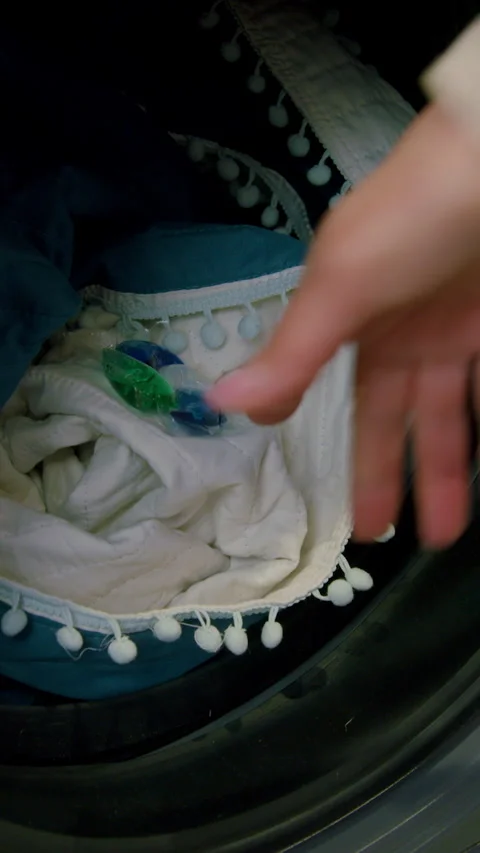 Hand placing laundry detergent pods into washing machine with blankets and Stock Footage 330020864