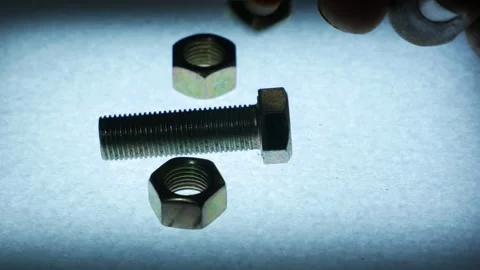 Hand Placing Metal Hex Nuts Around a Bolt on Textured Surface Stock Footage 340070214