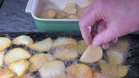 Hand placing more raw potato slices into a pan of hot oil. Vídeos de archivo 154408040