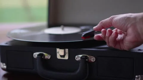 Hand placing needle on vinyl record on retro suitcase turntable close up Vídeos de archivo 340036180