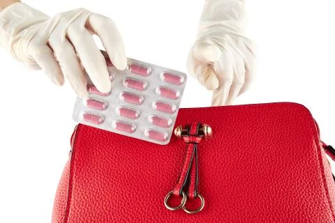 Hand placing package of pills in red leather womans bag. Isolated Foto stock
