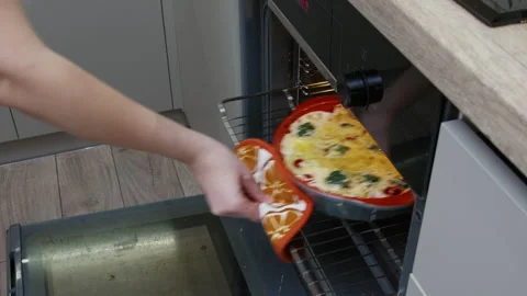 A hand placing a pan with eggs, cheese, tomatoes and spinach in an oven. Stock Footage 266423599