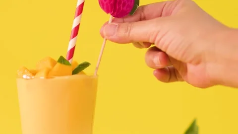 Hand Placing Paper Fruit Topper into Mango Smoothie with Striped Straw 库存影片 329460558
