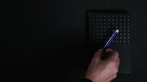 Hand placing pen on notebook on dark background Stock Footage 327288899
