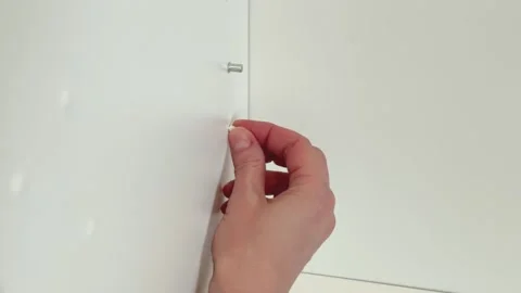 Hand placing plastic cap into unused shelf pin hole in white cabinet panel close Stock Footage 330933567