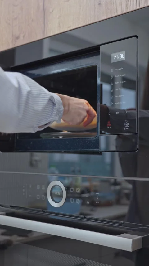 Hand placing plate into built in microwave oven in modern kitchen interior Stock Footage 331165003