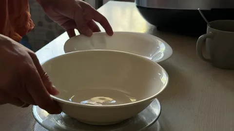 Hand placing plates on kitchen table in warm light. Simple domestic routine Stock Footage 336978369